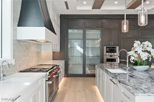 kitchen with dark brown cabinetry, sink, premium range hood, white cabinets, and appliances with stainless steel finishes