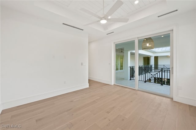 empty room featuring ceiling fan, light hardwood / wood-style floors, and a tray ceiling