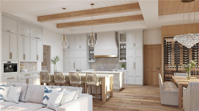 kitchen featuring hanging light fixtures, tasteful backsplash, light hardwood / wood-style flooring, a center island with sink, and custom range hood