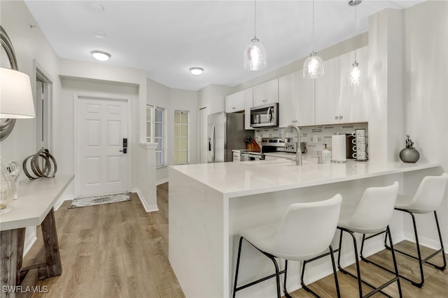 kitchen featuring kitchen peninsula, appliances with stainless steel finishes, a kitchen bar, decorative light fixtures, and white cabinets