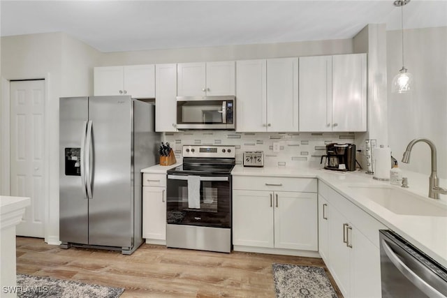 kitchen featuring pendant lighting, sink, light wood-type flooring, appliances with stainless steel finishes, and white cabinetry