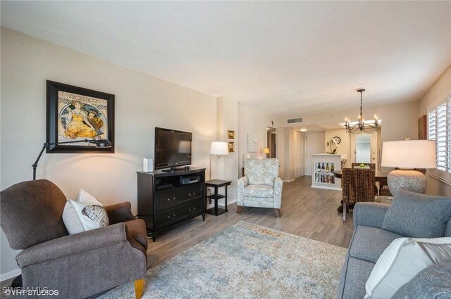 living room featuring visible vents, light wood-style flooring, baseboards, and an inviting chandelier