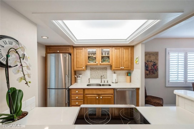 kitchen with a sink, light countertops, appliances with stainless steel finishes, brown cabinetry, and glass insert cabinets