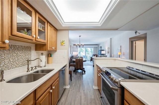 kitchen with stainless steel appliances, light countertops, glass insert cabinets, and a sink