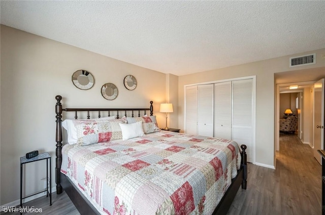 bedroom with a textured ceiling, visible vents, dark wood-style flooring, and a closet