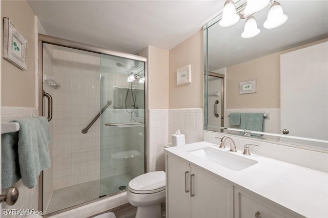 full bath featuring tile walls, toilet, a stall shower, wainscoting, and vanity