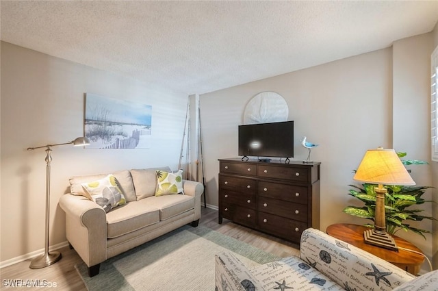 living area featuring light wood-type flooring, a textured ceiling, and baseboards