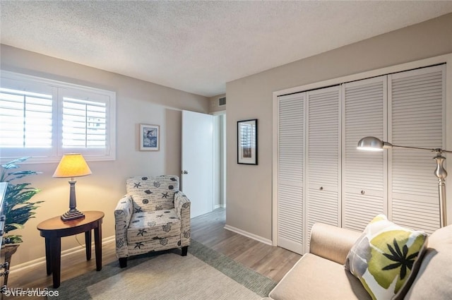 sitting room featuring baseboards, light wood-style flooring, visible vents, and a textured ceiling