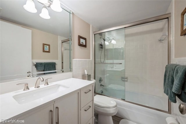 bathroom featuring tile walls, toilet, wainscoting, combined bath / shower with glass door, and vanity