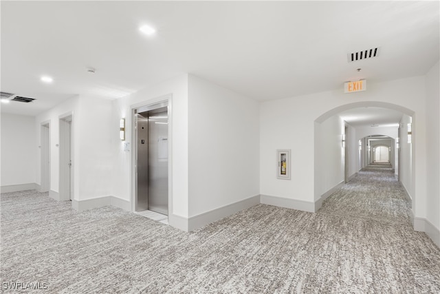 hall with elevator and light colored carpet