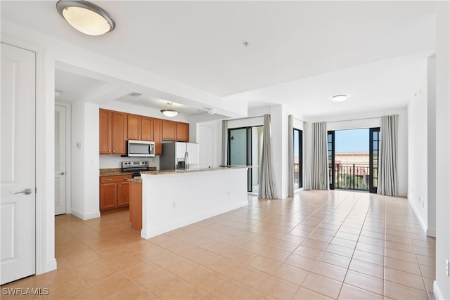 kitchen with appliances with stainless steel finishes, light stone counters, light tile patterned flooring, and an island with sink