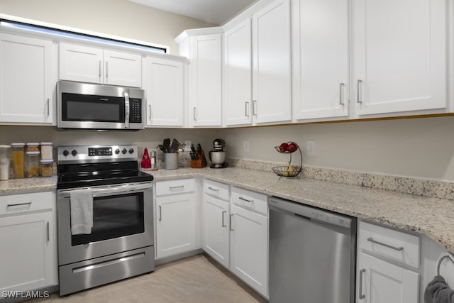 kitchen with appliances with stainless steel finishes, light stone counters, white cabinetry, and light tile patterned floors