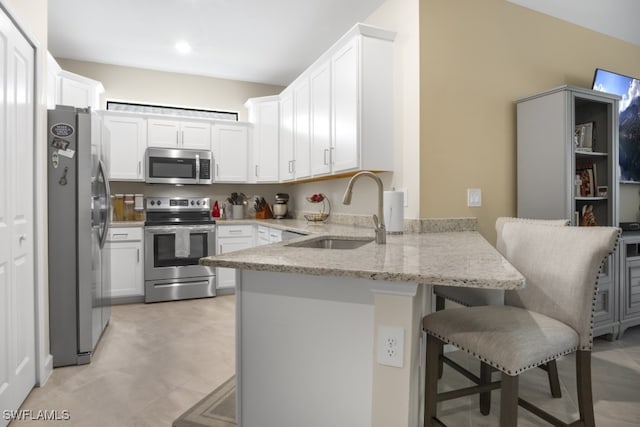 kitchen with sink, a breakfast bar, white cabinetry, appliances with stainless steel finishes, and light stone counters