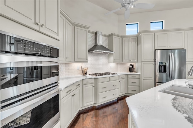 kitchen with light stone counters, wall chimney exhaust hood, white cabinetry, stainless steel appliances, and dark hardwood / wood-style floors