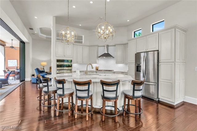 kitchen with pendant lighting, appliances with stainless steel finishes, wall chimney exhaust hood, and dark hardwood / wood-style floors