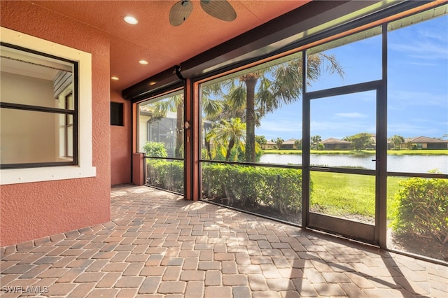 unfurnished sunroom featuring ceiling fan, a water view, and a wealth of natural light