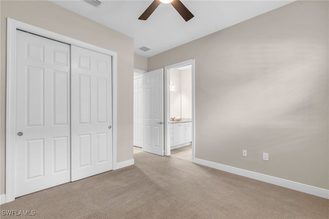 unfurnished bedroom with a closet, light colored carpet, ensuite bathroom, and ceiling fan