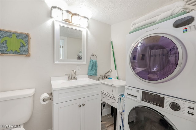 bathroom featuring a textured ceiling, toilet, vanity, stacked washing maching and dryer, and hardwood / wood-style flooring