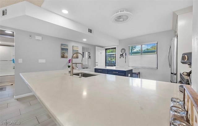 kitchen featuring blue cabinetry, stainless steel refrigerator, sink, a breakfast bar, and a kitchen island