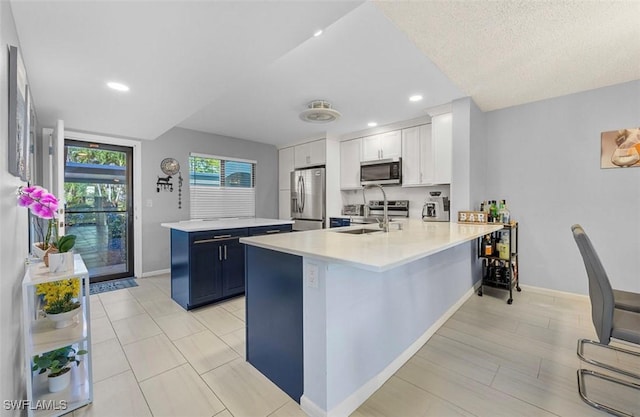 kitchen featuring kitchen peninsula, appliances with stainless steel finishes, a kitchen bar, blue cabinetry, and white cabinets