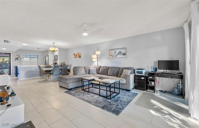 living room featuring a textured ceiling, light tile patterned flooring, and ceiling fan with notable chandelier