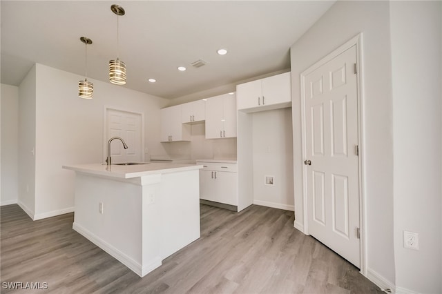 kitchen with light wood-type flooring, sink, white cabinetry, hanging light fixtures, and an island with sink