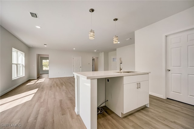 kitchen with white cabinets, sink, an island with sink, decorative light fixtures, and light hardwood / wood-style floors