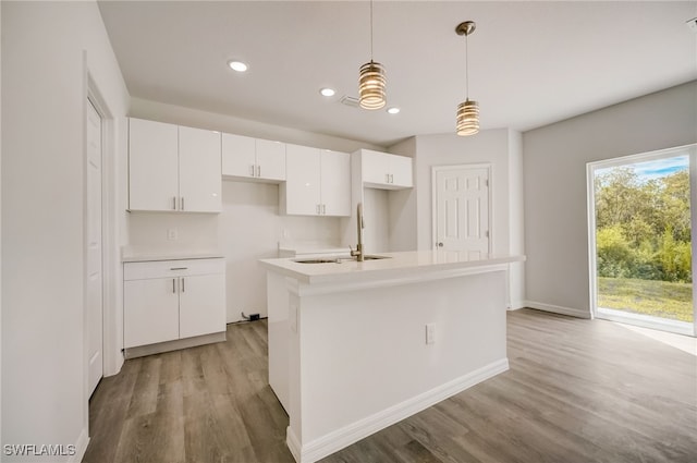 kitchen with sink, hanging light fixtures, light hardwood / wood-style floors, a kitchen island with sink, and white cabinets