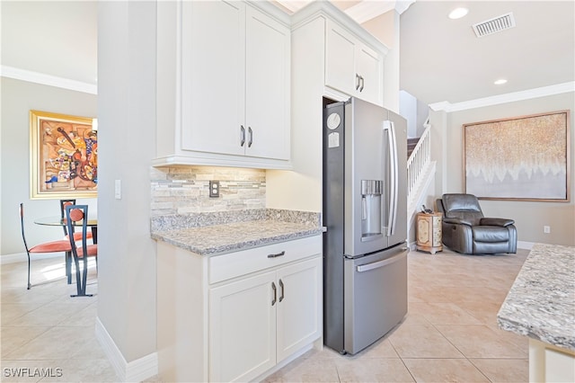 kitchen with backsplash, stainless steel fridge, crown molding, white cabinetry, and light stone counters