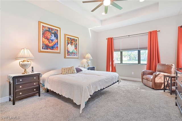 carpeted bedroom with ceiling fan and a raised ceiling