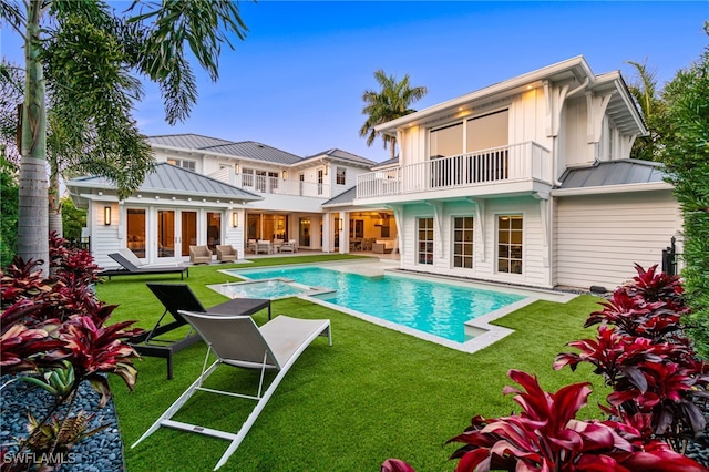 rear view of property featuring a patio, a lawn, a balcony, and french doors