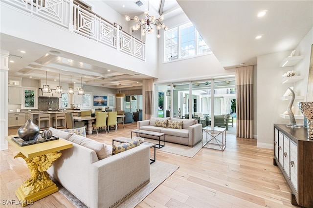 living room featuring beam ceiling, an inviting chandelier, light hardwood / wood-style flooring, a towering ceiling, and coffered ceiling