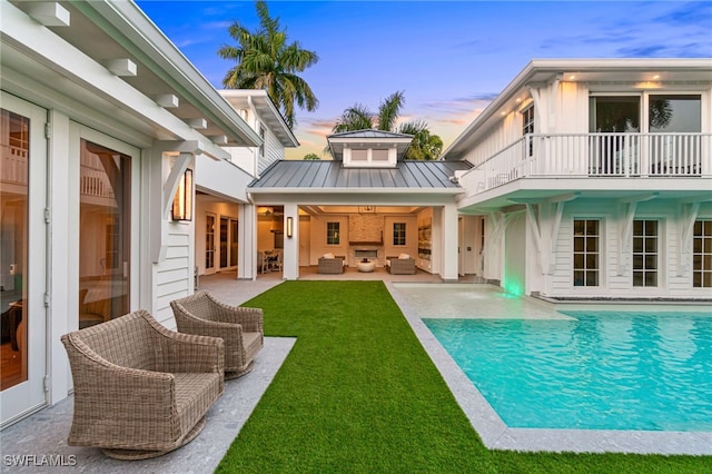 back house at dusk featuring a patio area, french doors, a lawn, and a balcony