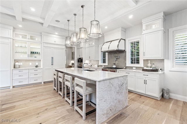 kitchen featuring beam ceiling, an island with sink, backsplash, and white cabinets