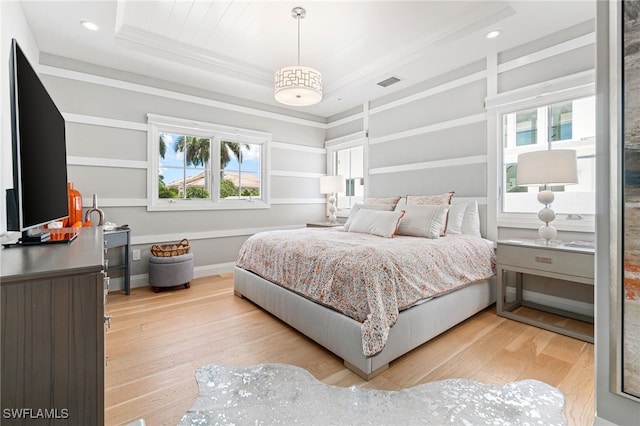 bedroom featuring crown molding, a tray ceiling, and light wood-type flooring