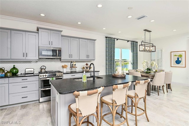 kitchen with hanging light fixtures, sink, a center island with sink, appliances with stainless steel finishes, and a breakfast bar area