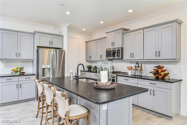 kitchen with ornamental molding, appliances with stainless steel finishes, sink, and a kitchen island with sink