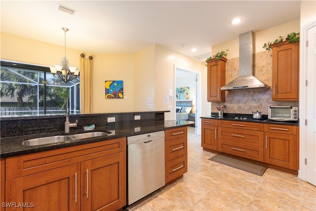 kitchen with dark stone counters, hanging light fixtures, wall chimney range hood, and stainless steel dishwasher