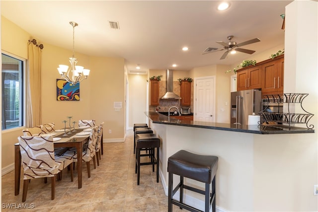 kitchen with tasteful backsplash, wall chimney exhaust hood, kitchen peninsula, decorative light fixtures, and high end refrigerator