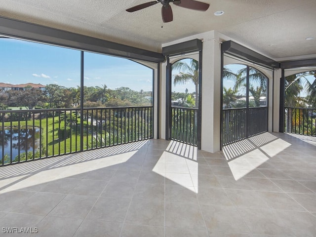 unfurnished sunroom featuring ceiling fan, a water view, and a wealth of natural light