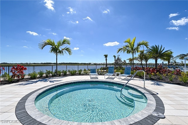 view of swimming pool featuring a patio, a water view, and a hot tub