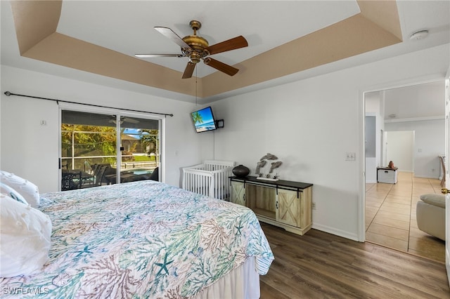 bedroom with wood-type flooring, access to outside, a tray ceiling, and ceiling fan