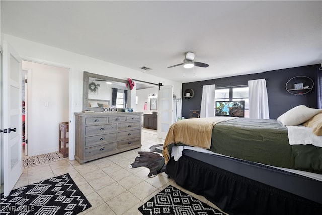 bedroom featuring light tile patterned floors, ceiling fan, ensuite bathroom, and a barn door