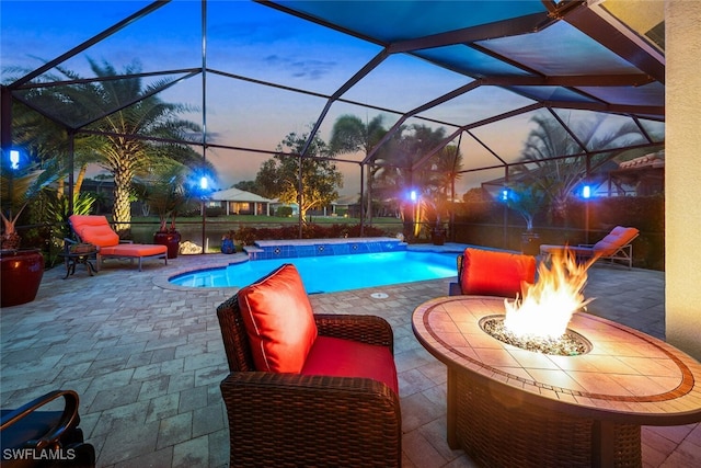 pool at dusk with glass enclosure, an outdoor fire pit, and a patio area