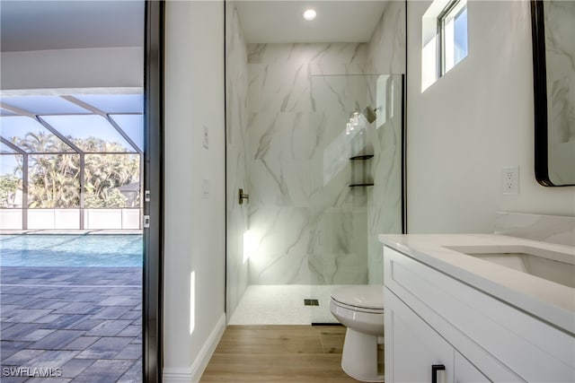 bathroom with wood-type flooring, tiled shower, vanity, and toilet