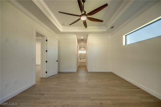 empty room featuring a raised ceiling, ornamental molding, light hardwood / wood-style flooring, and ceiling fan