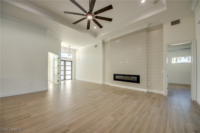 unfurnished living room with a fireplace, crown molding, a tray ceiling, and light wood-type flooring