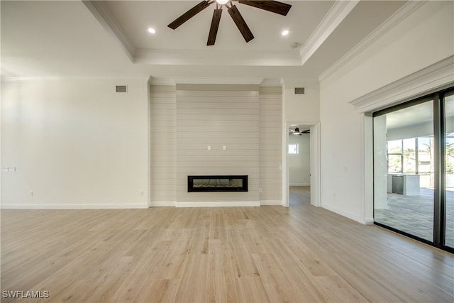 unfurnished living room with ceiling fan, a tray ceiling, light hardwood / wood-style flooring, a fireplace, and ornamental molding