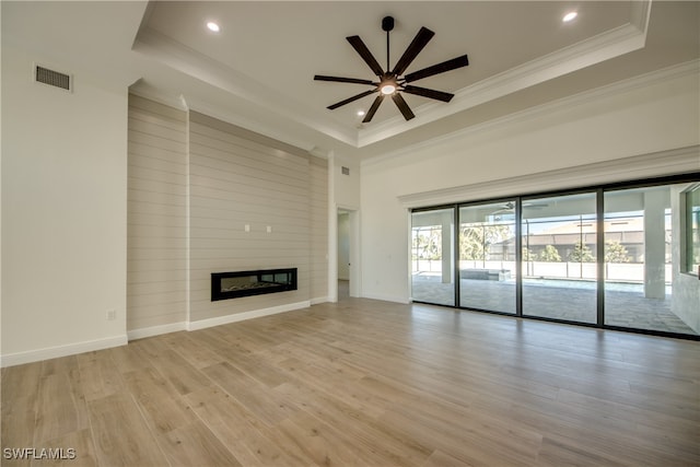 unfurnished living room featuring ceiling fan, a raised ceiling, a fireplace, crown molding, and light hardwood / wood-style floors