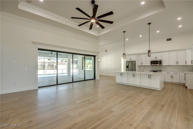 kitchen with pendant lighting, white cabinets, a raised ceiling, a center island with sink, and stainless steel appliances